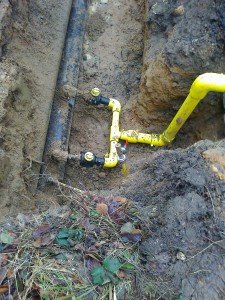 Yellow pipes and valves exposed below the surface of the road
